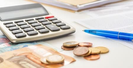 A calculator, pen, and coins on a desk.